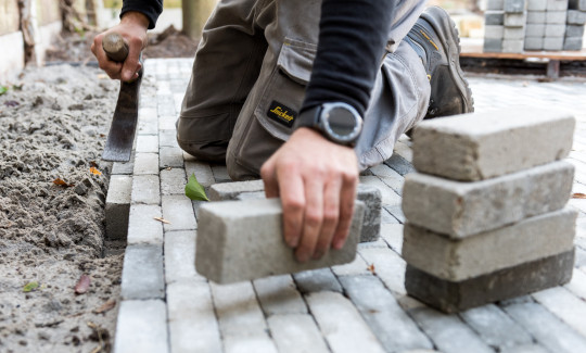 Hovenier plaatst betonklinkers langs de rand van een nieuw aangelegd pad en klopt ze aan met een hamer.