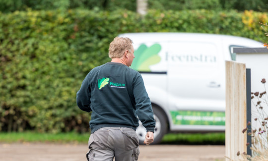 Hovenier loopt over oprit richting woning in Putten, met een Feenstra-busje op de achtergrond.